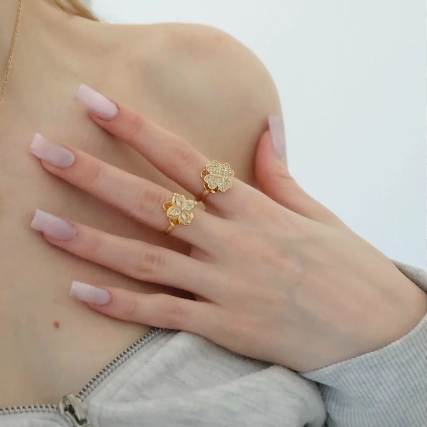 Gold flower-shaped earrings on a hand with light pink nail polish against a neutral background