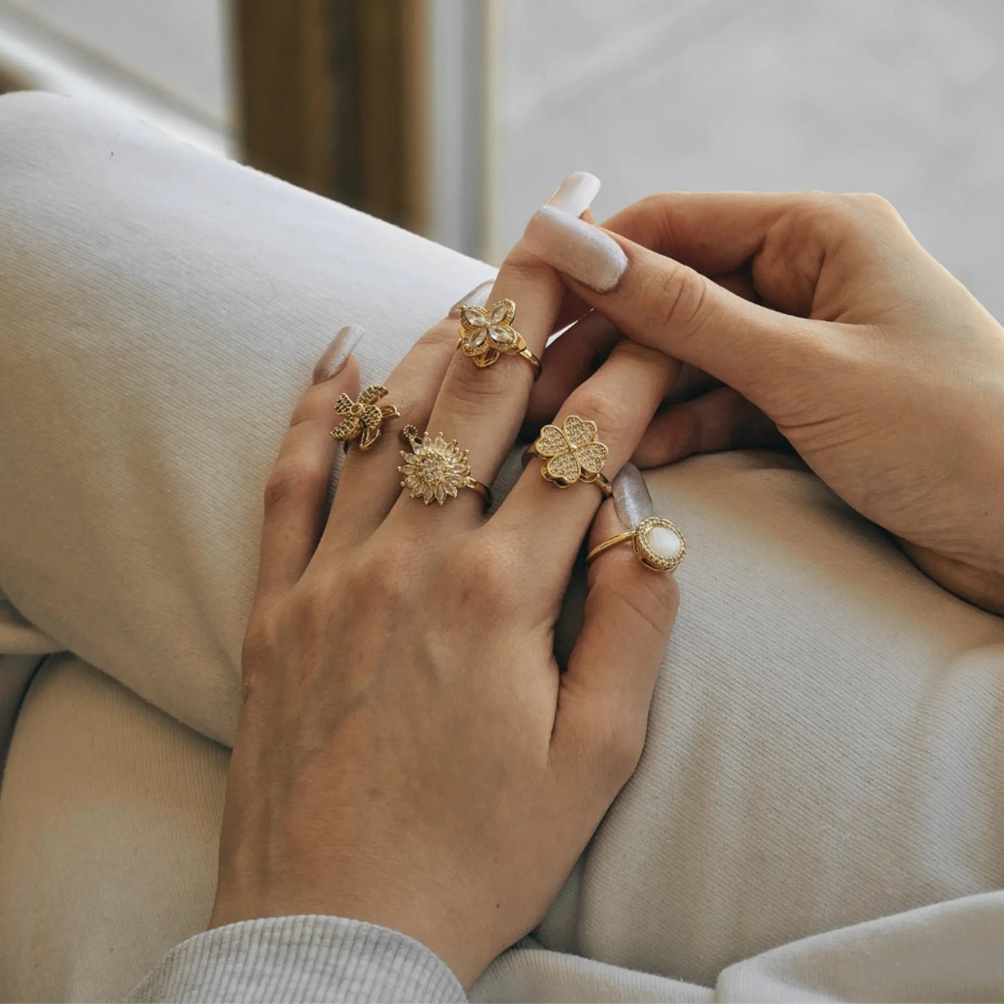 Close-up of hands wearing gold rings with a neutral background
